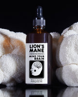 MindRise Lion's Mane Extract dropper bottle with the Mind Your Brain label, between fresh Lion's Mane mushrooms